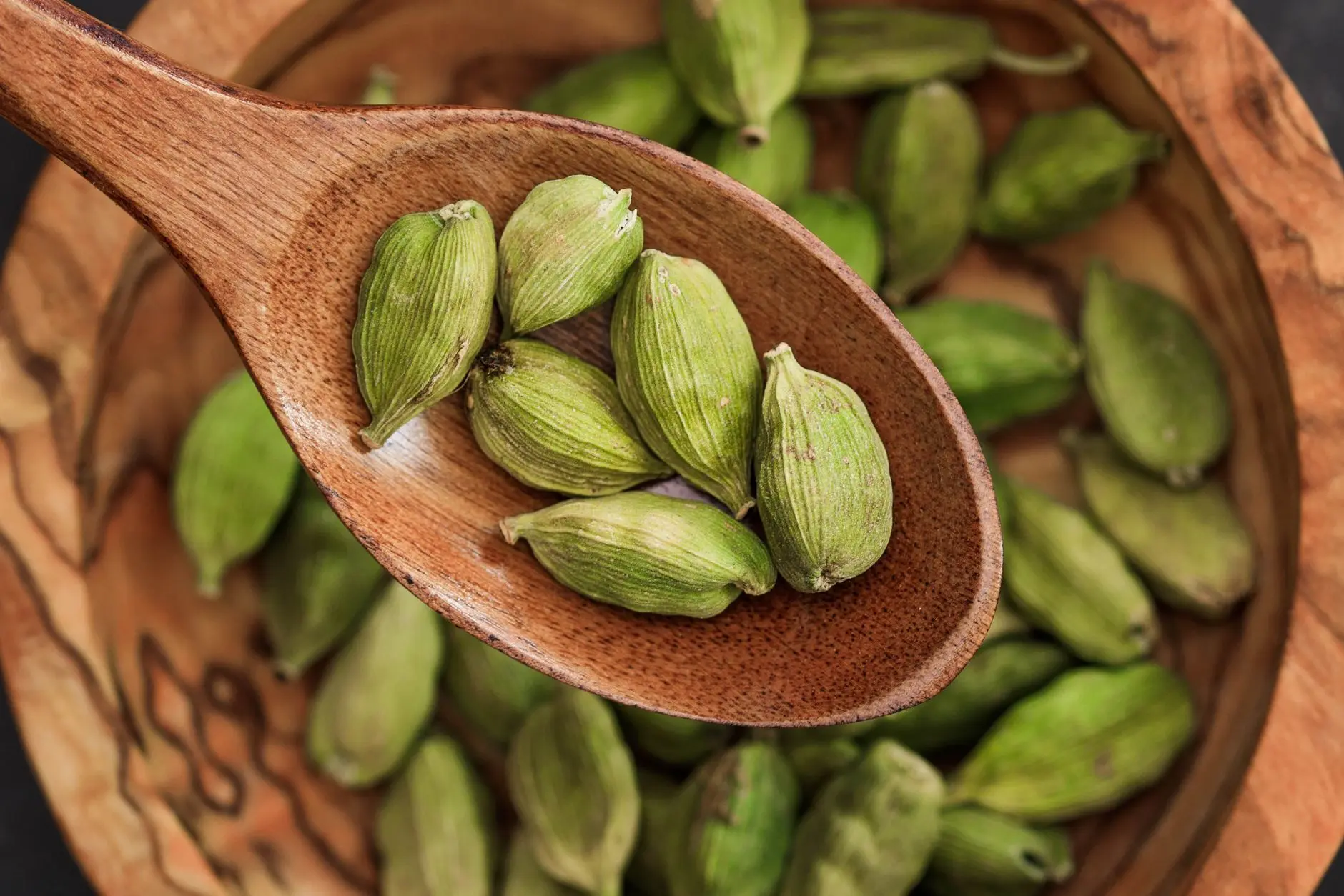 wooden spoon holding whole cardamom over bowl