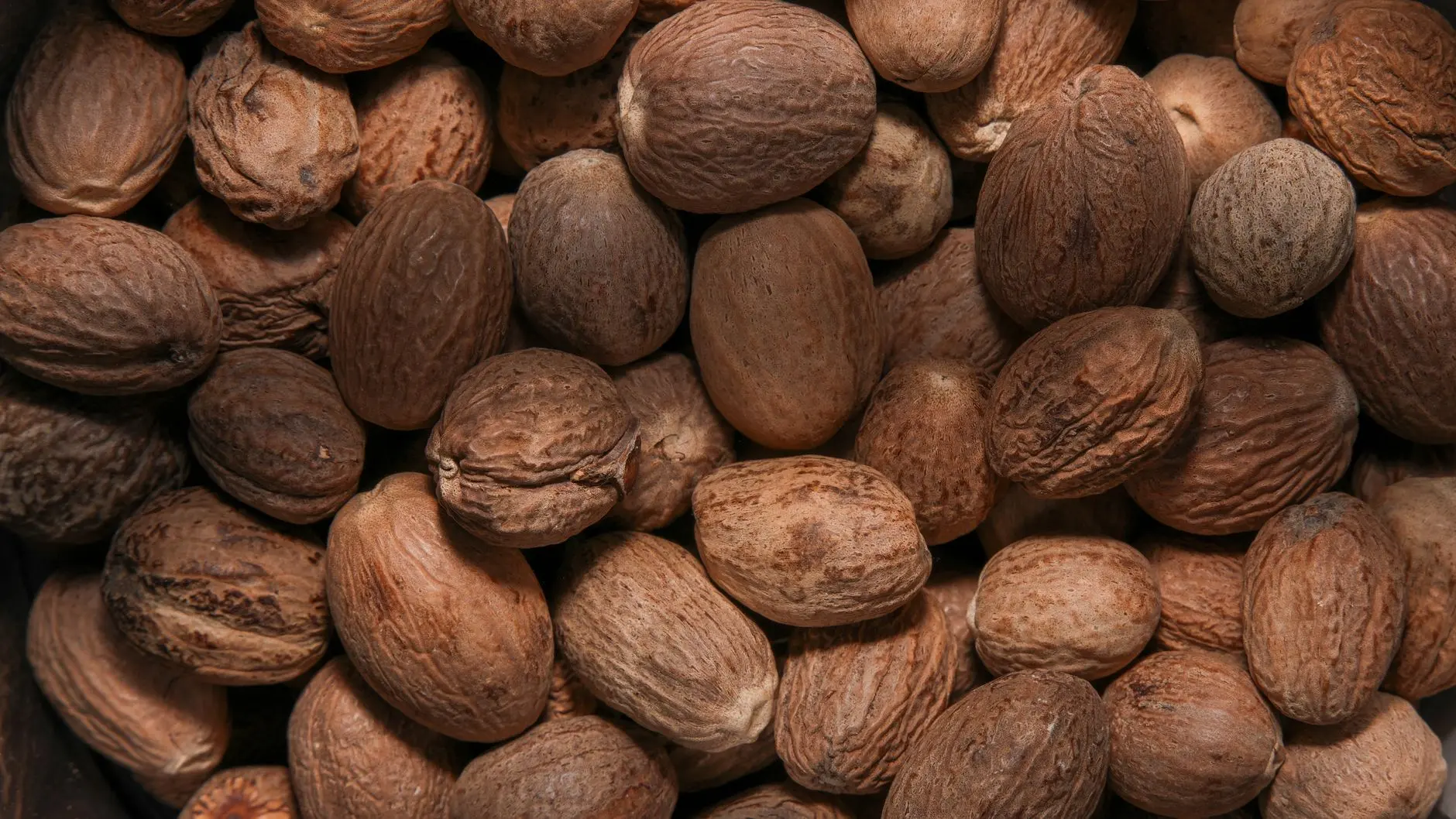 many whole nutmeg seeds filling the frame, flatlay