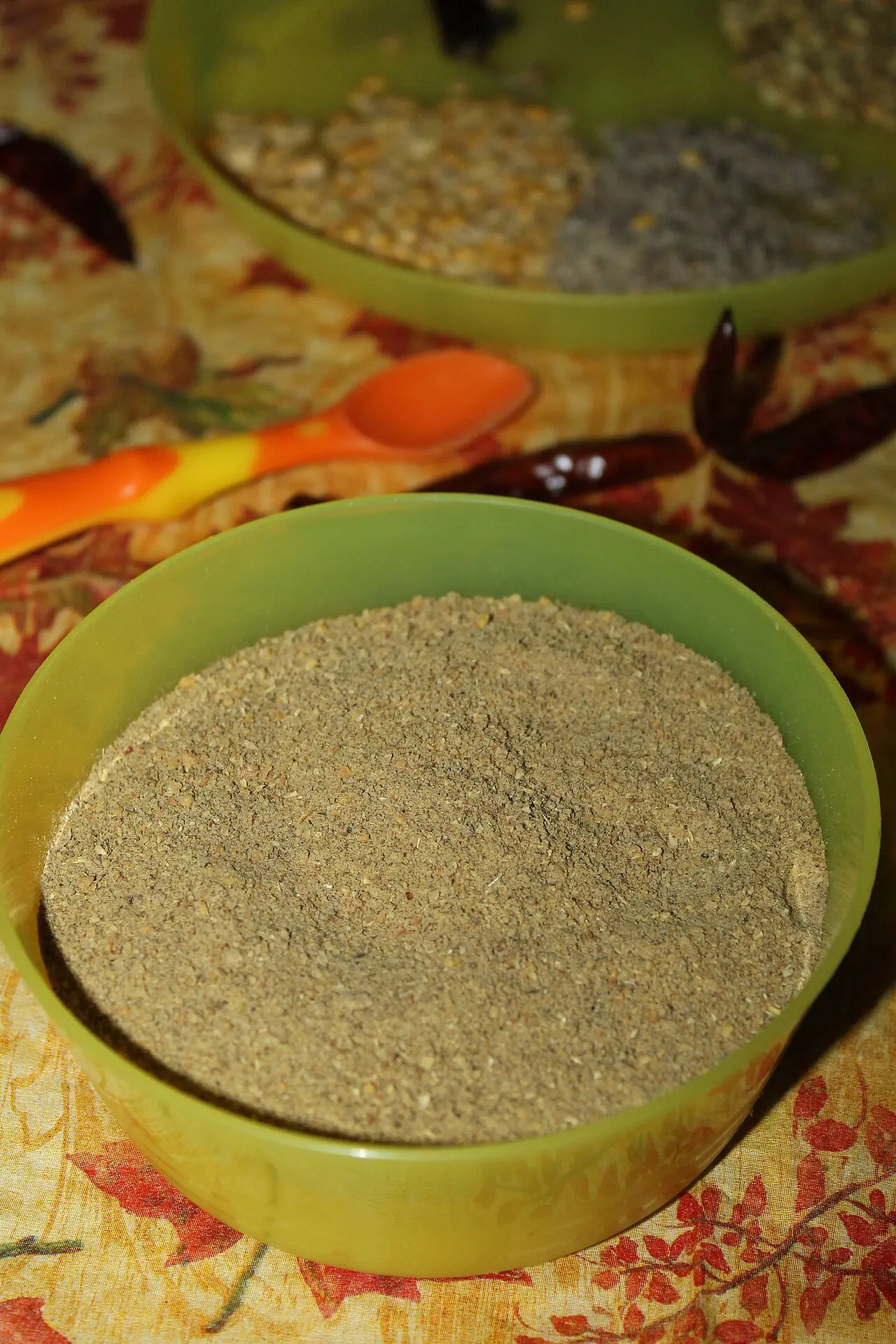 green bowl filled with coarse brown spice powder, tablecloth background