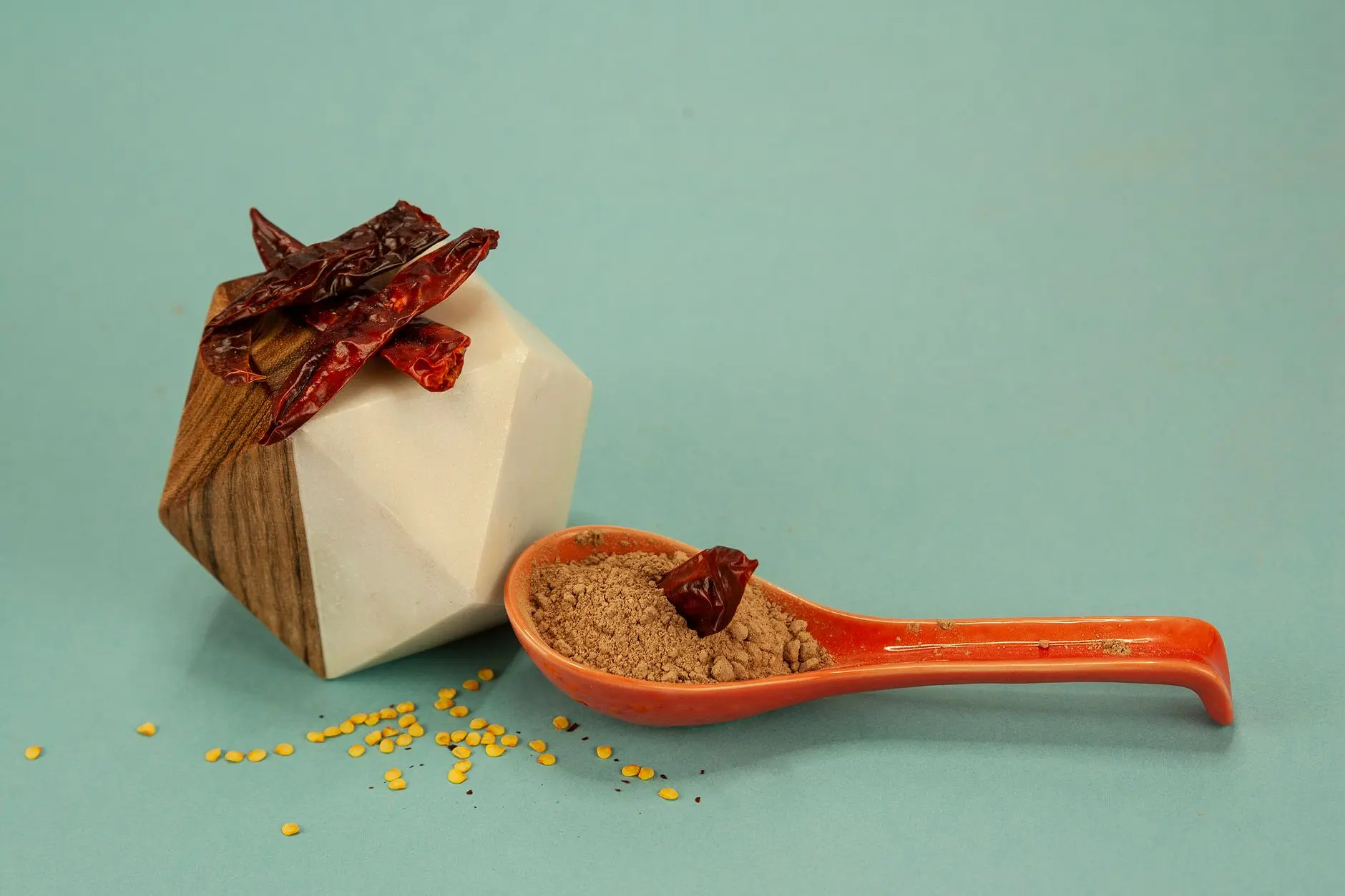 spoon of brown spice powder with dried chilies on teal background